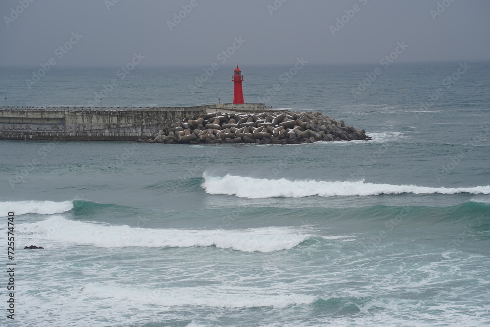A red lighthouse standing in the middle of the bitter waves and winter sea
