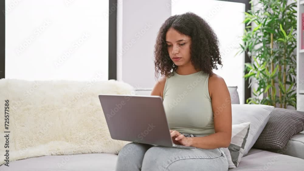 Devoted young hispanic woman embraced by cozy home atmosphere, deeply engrossed in high-tech world, beautifully focused on laptop while comfortably sitting on sofa in well-lit living room. Devoted young hispanic woman embraced by cozy home atmosphere, deeply engrossed in high-tech world, beautifully focused on laptop while comfortably sitting on sofa in well-lit living room.