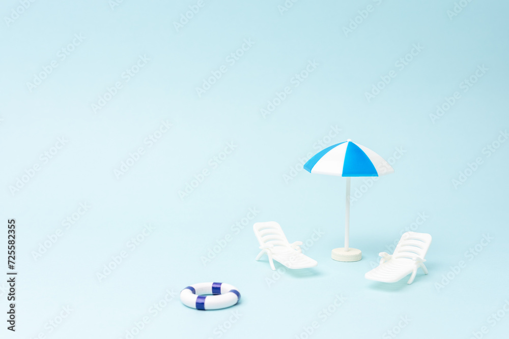 Summer background with sunbeds, sun umbrella and swimming ring on pastel blue background. Creative holiday concept.