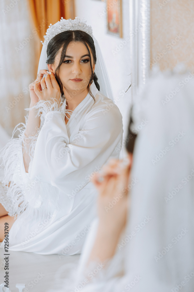 Beautiful, young, perfect model bride in a white lace dress sits in the room, bedroom in the morning, putting an earring on her ear. Wedding photography, portrait, concept. Beautiful, young, perfect model bride in a white lace dress sits in the room, bedroom in the morning, putting an earring on her ear. Wedding photography, portrait, concept.