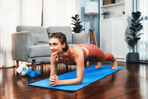 Athletic and sporty woman doing plank on fitness mat during home body workout exercise session for fit physique and healthy sport lifestyle at home. Gaiety home exercise workout training.