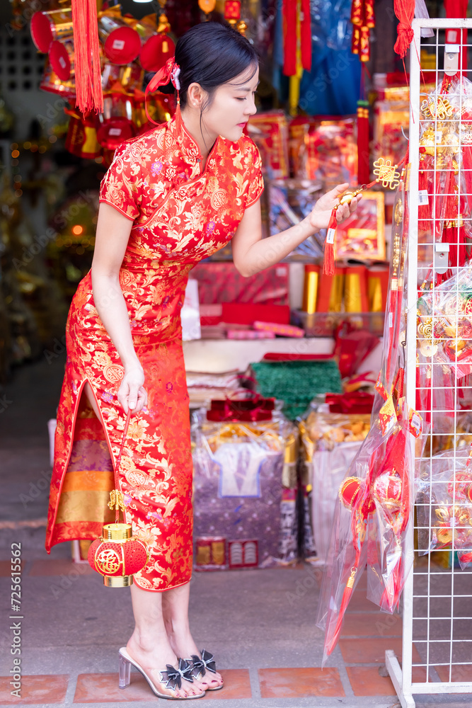 Asian woman in red cheongsam dress choosing and buying home decoration and ornament for celebrating Chinese Lunar New Year festival at market.Celebrate Chinese lunar new year.Celebrate season holiday.