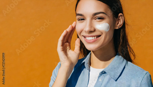 Beautiful young woman with sun protection cream on her face against orange background, closeup. Space for text