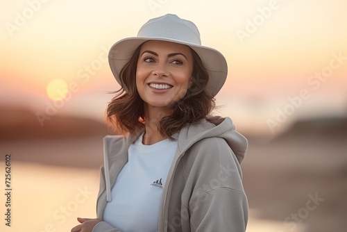 Beautiful young woman wearing hat and coat on the beach at sunset