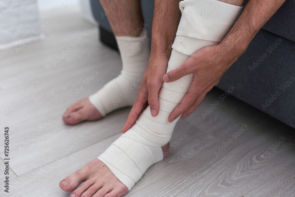 Man bandaging injured ankle. Injury leg. First aid for sprained ligament or tendon Man bandaging injured ankle. Injury leg. First aid for sprained ligament or tendon