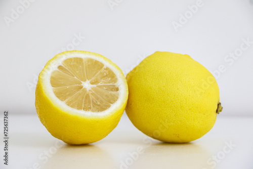 A full lemon and a half-sliced lemon showing it’s texture and cross-section pattern, on white background, lemons are citrus fruits known for their sour juicy taste and health benefits