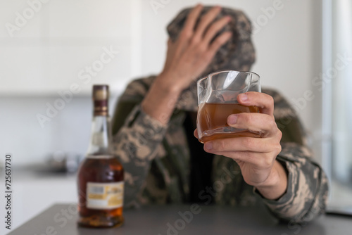A man in camouflage suffers from depression after returning from the army. He uses alcohol and narcotic tablets. He is tormented by heavy memories. On the table is a gun.