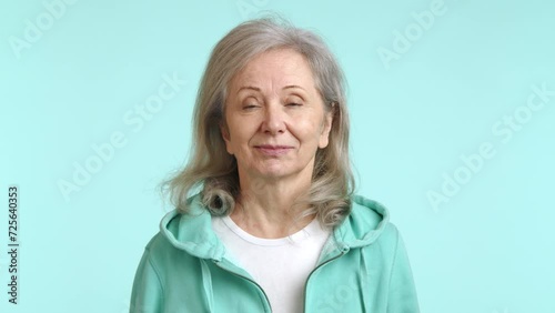 A smiling elderly lady wearing a refreshing mint-colored hoodie, playfully gesturing 'call me' with her hand against a soft blue background. Ideal for contact us themes. Camera 8K RAW. photo