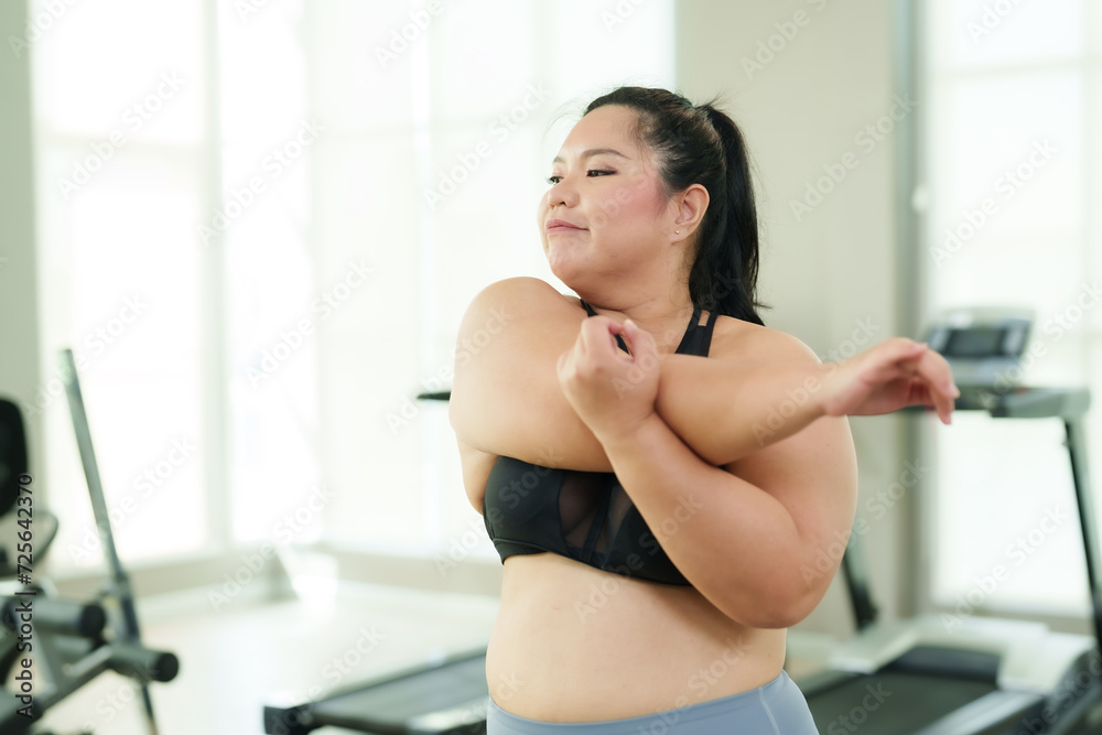 Plus-size Asian woman exercise in gym, gear stretching arms, feeling relaxed and accomplished after workout, with treadmills behind. Content female in sportswear arm stretches, enjoying her fitness Plus-size Asian woman exercise in gym, gear stretching arms, feeling relaxed and accomplished after workout, with treadmills behind. Content female in sportswear arm stretches, enjoying her fitness