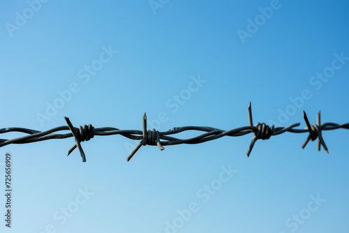 Close-up of Barbed Wire Against Clear Sky. A detailed close-up of rusty barbed wire, with a clear and expansive blue sky in the background, symbolizing restriction.