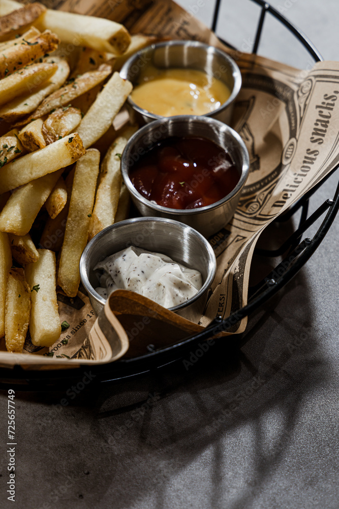 Fototapeta premium French fries with ketchup and mayonnaise in a basket on a gray background