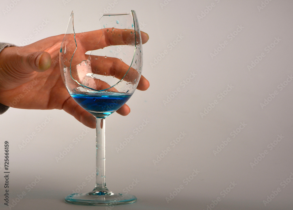 niebieski płyn w peknietym kieliszku do wina, dłoń trzymajaca pęknięty kieliszek, blue liquid in broken wine glass, hand holding broken wine glass,hand with broken wine glass with blue liquid - obrazy, fototapety, plakaty 