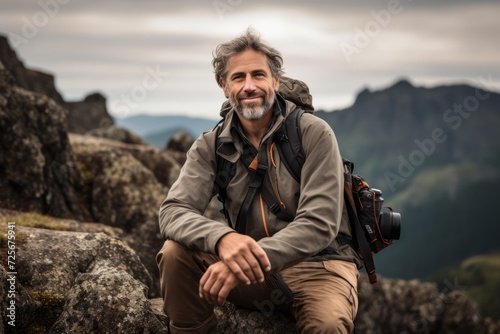 Handsome senior man with backpack and camera sitting on top of a mountain