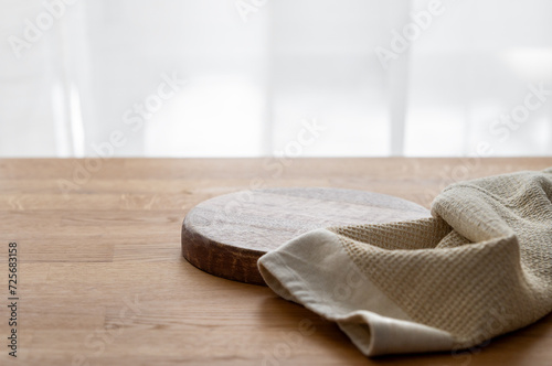 Fototapeta Naklejka Na Ścianę i Meble -  Empty cutting board on wooden texture tabletop with kitchen towel in front of window.