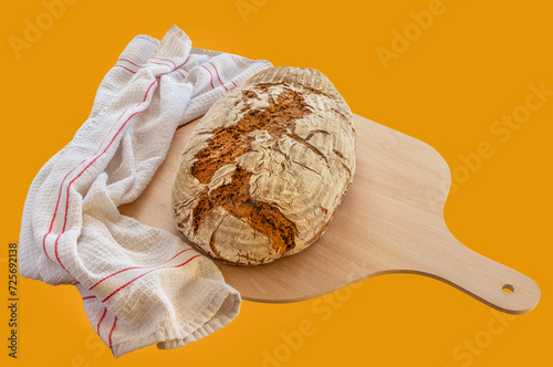 Frisch gebackenes Brot auf einer Holzschaufel mit Geschirrtuch vor einem braunen Hintergrund
