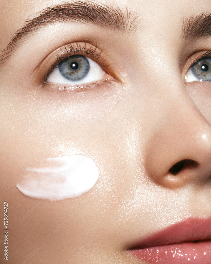 Fototapeta premium Rejuvenation,moisturizer and skin care. Close up portrait of a beautiful model with a skincare cream smear on the face. Dermatology cosmetics products