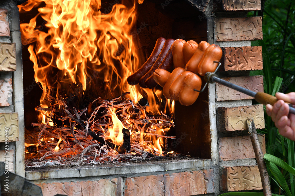 Detail on the roasting sausage on natural fire at cottage in home fireplace at grill party