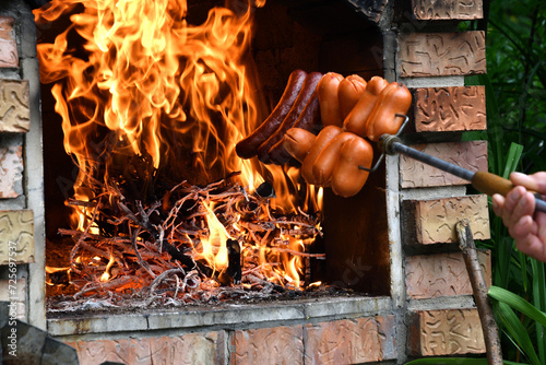 Obraz na płótnie Detail on the roasting sausage on natural fire at cottage in home fireplace at grill party w salonie