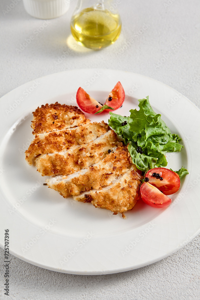 Golden crusted chicken fillet with cheese on a bed of lettuce, topped with cherry tomatoes, ideal for recipes and menu designs