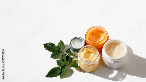 Skin care cosmetics. Composition of a different containers with natural herbal moisturising products scrub, cream, peeling, green tea tree lotion and chea butter, top view, white background