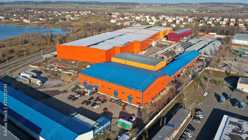 Aerial drone view of a large orange-colored logistics center, a storage warehouse for big retail chains on the shores of a blue lake in Europe, America. Storage warehouses near the city.