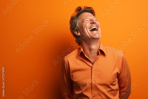 Portrait of a happy young man laughing over orange background. Studio shot