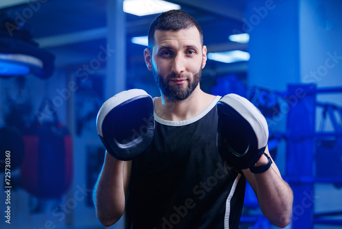 Male boxer instructor holds gloves for practicing punches in boxing ring, blue toning. Concept sport gym training © Parilov