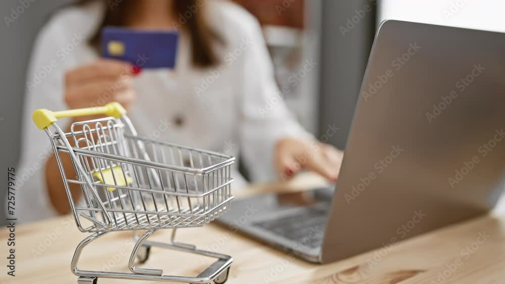 A young woman with brunette hair shops online with a credit card at an office, hinting at e-commerce and consumerism. A young woman with brunette hair shops online with a credit card at an office, hinting at e-commerce and consumerism.