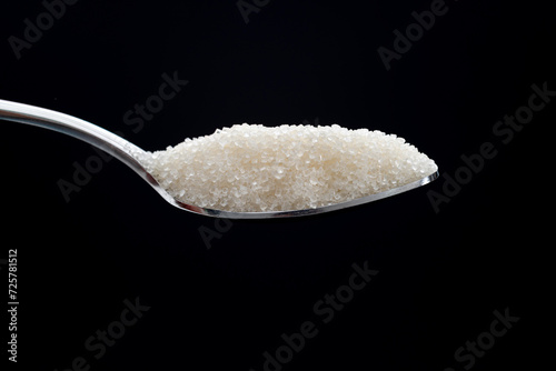 Spoon with sugar crystals on black background
