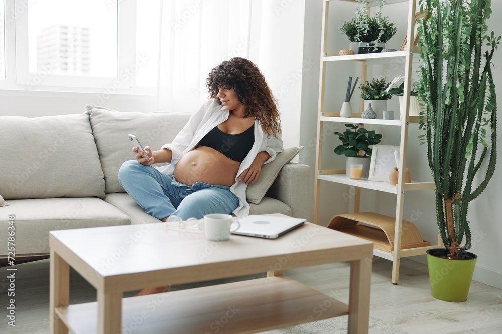 Pregnant woman blogger sits on the couch at home and takes pictures of herself on the phone