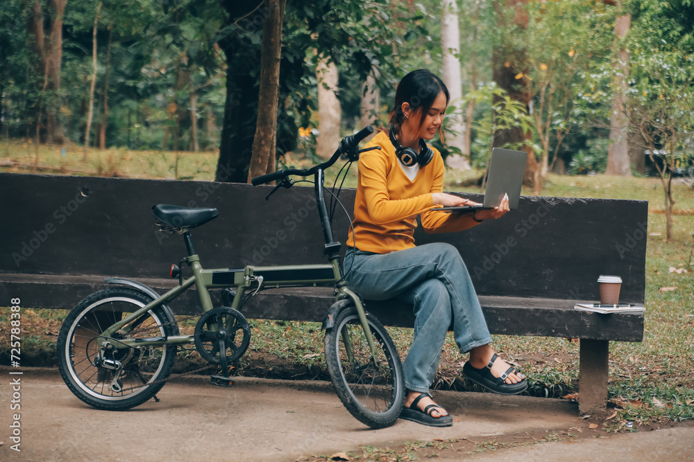 Happy young Asian woman while riding a bicycle in a city park. She smiled using the bicycle of transportation. Environmentally friendly concept. Happy young Asian woman while riding a bicycle in a city park. She smiled using the bicycle of transportation. Environmentally friendly concept.