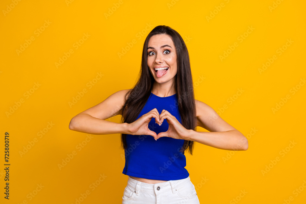 Photo of positive funky lady dressed blue top stick out shoeing arms heart isolated yellow color background Photo of positive funky lady dressed blue top stick out shoeing arms heart isolated yellow color background