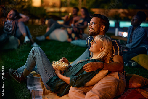 Young couple eating popcorn while watching movie at night in backyard. photo