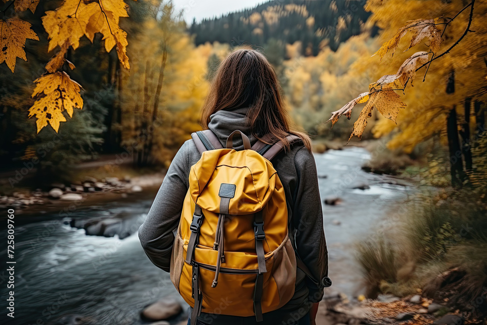 Golden Journeys: active woman adorned with a bright yellow backpack finds solace as she gazes at flowing river, embracing natures allure. Golden Journeys: active woman adorned with a bright yellow backpack finds solace as she gazes at flowing river, embracing natures allure.