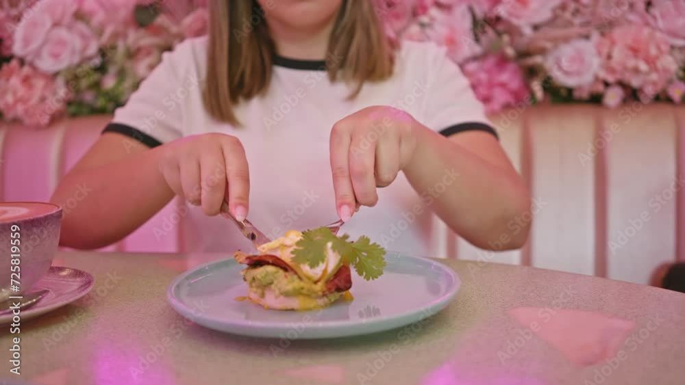 A woman prepares to eat eggs benedict in a stylish cafe with pink floral decor. A woman prepares to eat eggs benedict in a stylish cafe with pink floral decor.