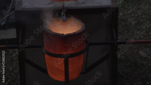 A large crucible filled with molten bronze is brought with a metal basket to pour into a mold