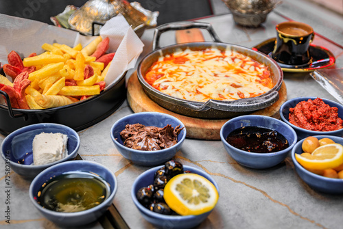 Traditional Turkish breakfast kahvalti with eggs in a skillet, jams, olives, cheese, dips, fries and Turkish coffee at a restaurant, Istanbul, Turkey photo