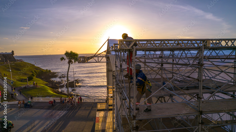 Naklejka premium Workers assembling metal structure with the ocean and sunset in the background