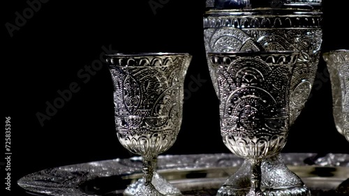 A side closeup of a silverware set, with handmade cultural and traditional South Asian designs, rotating on an automatic display stand in a black background and cinematic indoor light.  photo