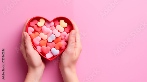 Female hands take candy from a heart-shaped box, top view, empty space. Gift for Valentine's Day. Hands with a package of sweets