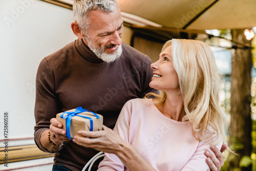 Mature attractive man husband giving his blonde smiling wife a gift in their garden. Anniversary concept. Receiving gifts - love language photo