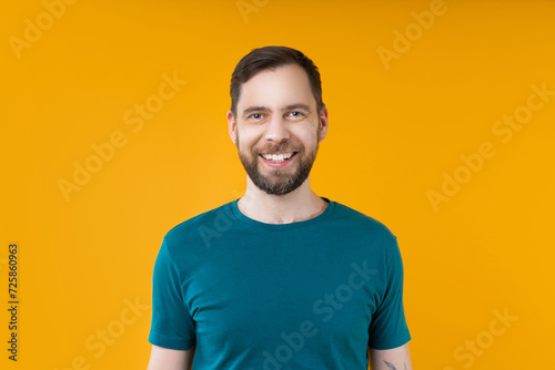 Close up studio shot of young attractive smiling bearded man posing over bright colored orange yellow background