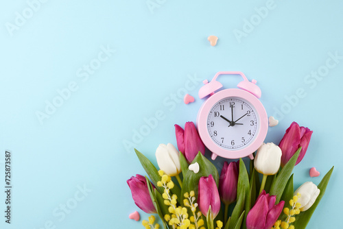 It's time to commemorate International Women's Day. Top view photo of alarm clock, hearts, tulips, mimosa on pastel blue background with space for festive message