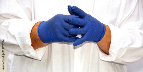 Medic hands in blue nitrile gloves. The doctor puts on sterile gloves against the background of a medical gown. The doctor puts on sterile gloves against the background of a medical gown. © Helen-HD