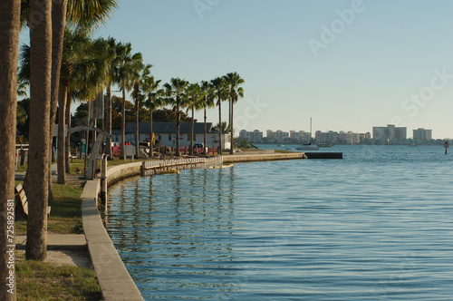 Wide view from Gulfport , Florida Marina looking west with s curve of concrete seawall towards Boca Ciega Bay in afternoon sun. Green Palm trees on the side with calm water and blue sky.