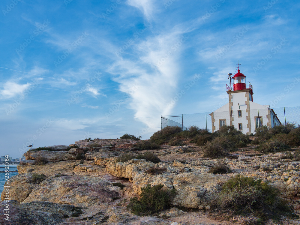 Farol da Ponta do Altar.Lighthouse in Ferragudo, Lagoa, Portugal. Lighthouse on a rocky elevation, blue sky and the city of Portimão in the background.