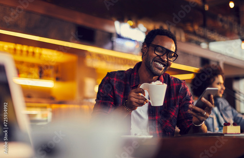 Young man using a smart phone while enjoying a coffee at a cafe photo