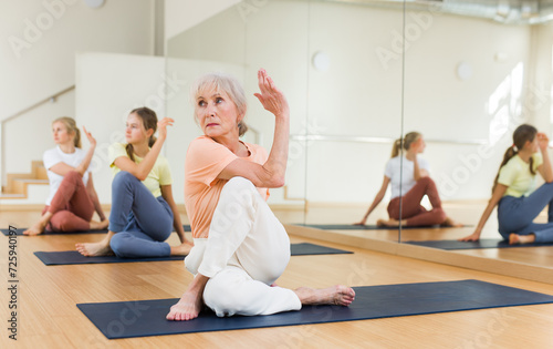 Elderly woman sitting on mats in lord of fishes pose while training yoga with her family.