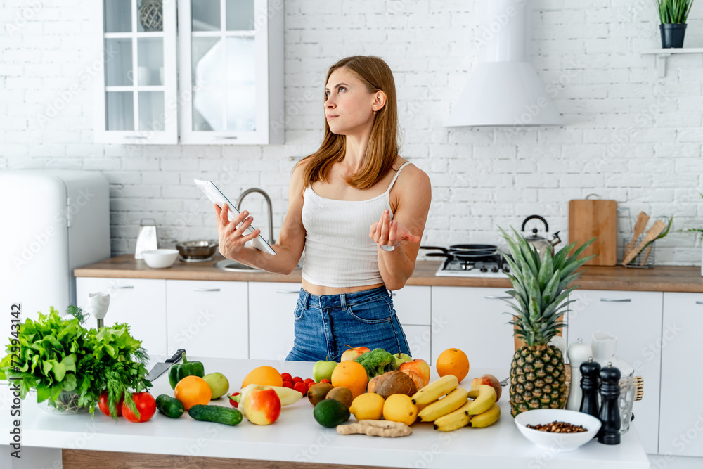 Young woman standing in the kitchen with smartphone and fresh fruits Young woman standing in the kitchen with smartphone and fresh fruits