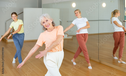 Portrait of cheerful active female pensioner exercising dance moves in fitness studio